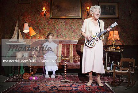 Older woman playing guitar as girl knits