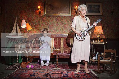 Older woman playing guitar as girl knits