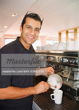 Man pouring foamed milk into coffee cup