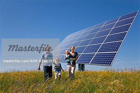 Family walking in field by solar panel