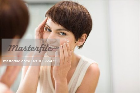 Woman applying moisturizer in mirror