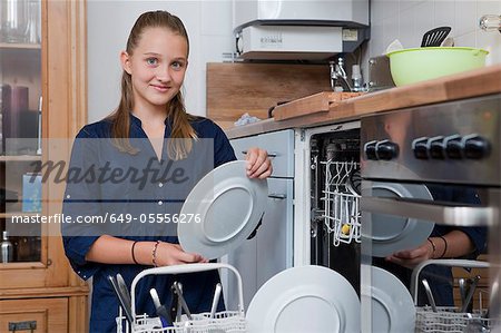 Smiling girl loading dishwasher
