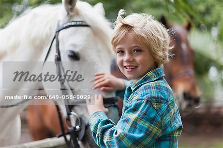 Smiling boy petting horse in yard
