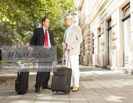Businessmen rolling luggage outdoors