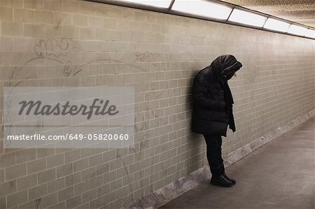 Hooded person leaning on subway wall Hooded person leaning on subway wall