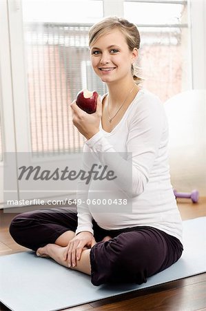 Pregnant woman eating apple on yoga mat