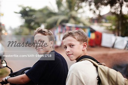 Teenage boys riding scooter on dirt road