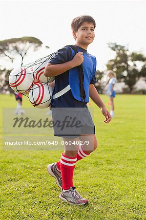 Boy carrying soccer balls on pitch