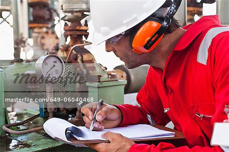 Worker noting gauge at oil refinery Worker noting gauge at oil refinery