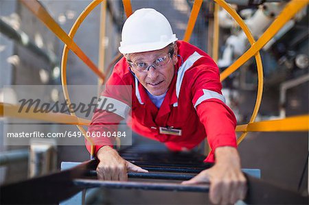 Worker climbing ladder at oil refinery