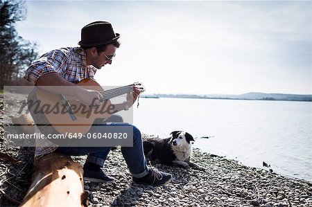 Man playing guitar with dog by creek
