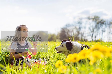 Girl blowing bubbles with dog in field Girl blowing bubbles with dog in field