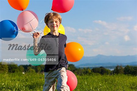 Boy with colorful balloons in grass