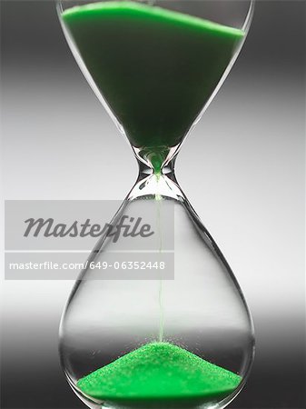 Green sand pouring through hourglass