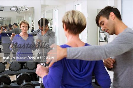Trainer adjusting woman's form in gym