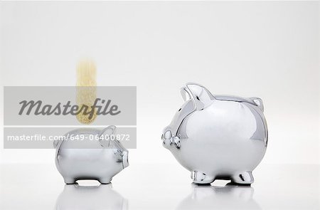 Coin dropping into smaller piggy bank Coin dropping into smaller piggy bank