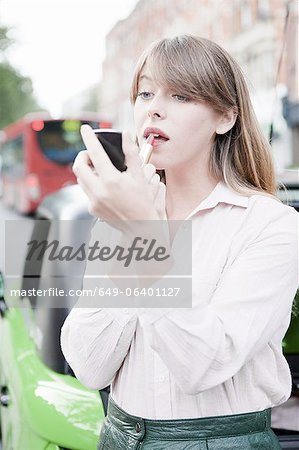 Woman applying lipstick on city street