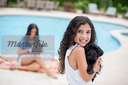 Smiling girl holding puppy by pool