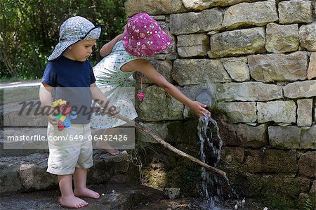 Children playing at water spout in wall
