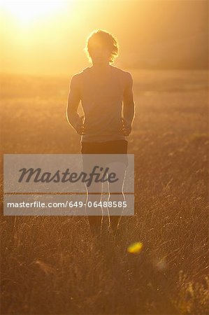 Man running in tall grass at sunset