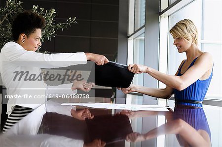 Businesswomen fighting over folder Businesswomen fighting over folder
