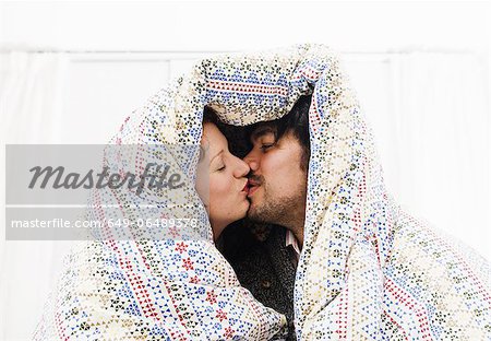 Couple kissing under duvet blanket