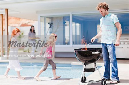 Girls around pool as father grills