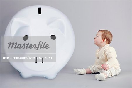 Baby girl examining large piggy bank