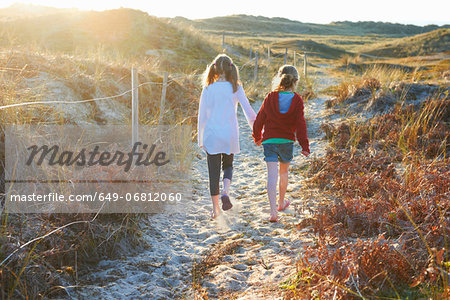 Two girls walking on path in sand dunes rear view