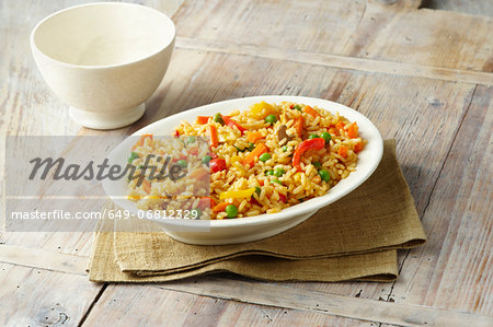 Savoury rice with, peas, red and yellow peppers, carrots and mushrooms in white serving dish