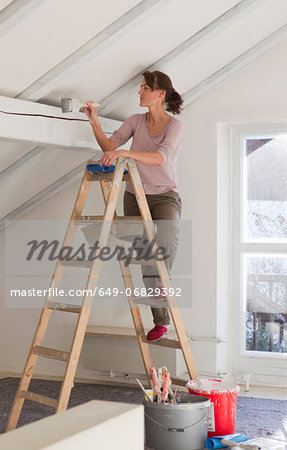 Woman on stepladders painting white ceiling