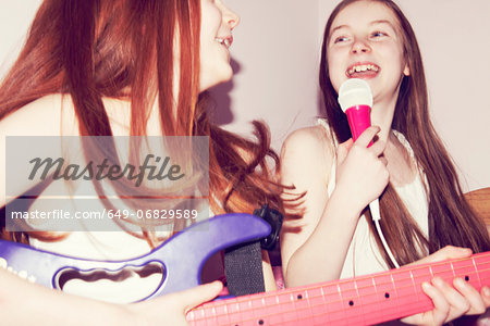 Two girls playing guitar and singing into microphone in bedroom