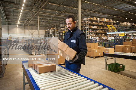 Male warehouse worker selecting cardboard boxes from conveyor belt