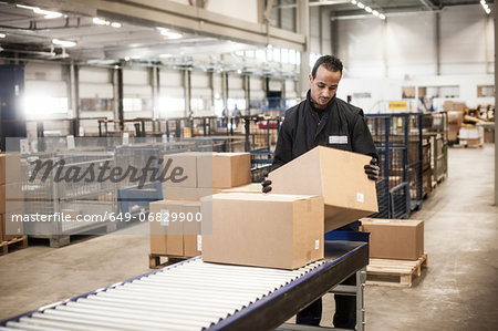 Male warehouse worker checking cardboard box from conveyor belt