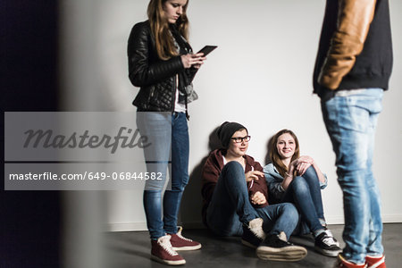 Two teenagers sitting on floor with people standing in foreground