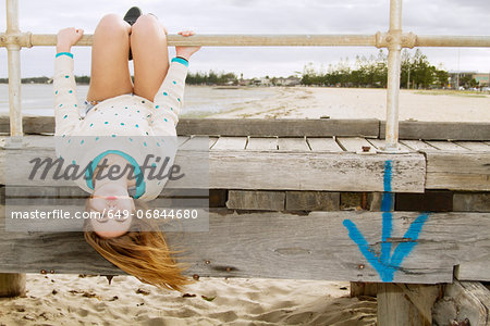 Young woman hanging upside down from pier