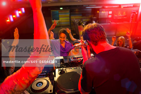 Rear view of disc jockey surrounded by people dancing