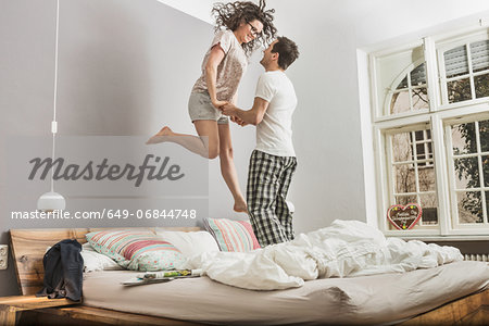 Mid adult couple wearing pyjamas jumping on bed