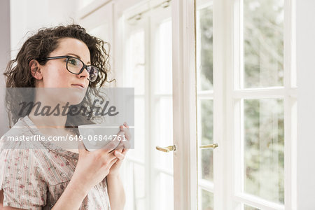 Mid adult woman holding coffee cup, looking out of window