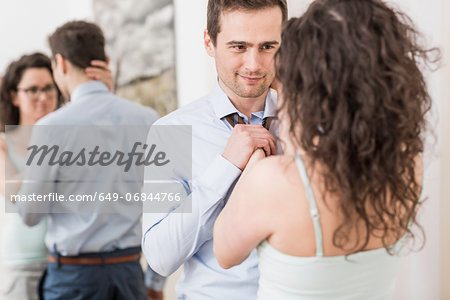 Mid adult woman helping man to fasten tie