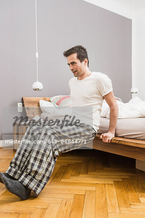 Mid adult man wearing pyjamas doing exercise on bed