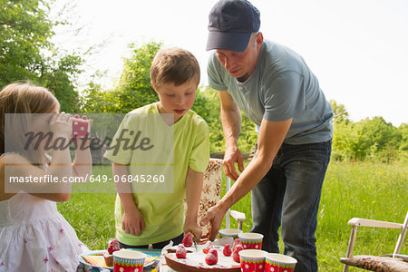 Father with two children cutting birthday cake outdoors