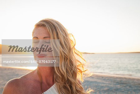 Blond woman with eyes closed on beach at dusk, Cape Town, South Africa