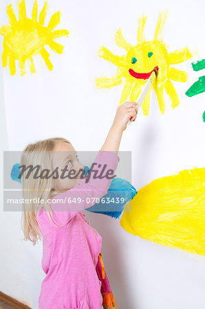 Young girl painting smiling sunshine on wall