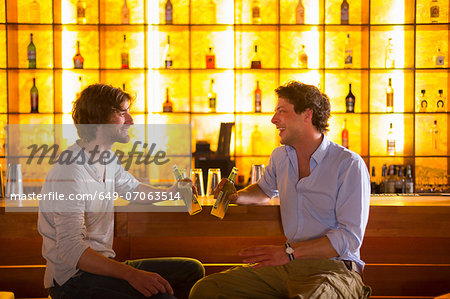 Two men sitting at bar with bottles of beer
