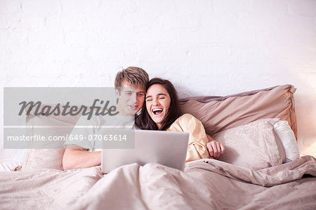 Young couple watching laptop in bed