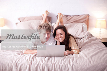 Young couple lying on bed watching laptop