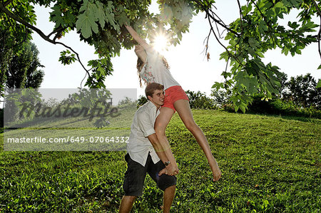 Young man lifting young woman to tree branches
