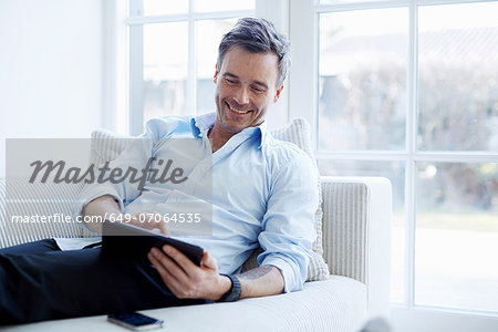 Man relaxing on sofa using digital tablet Man relaxing on sofa using digital tablet