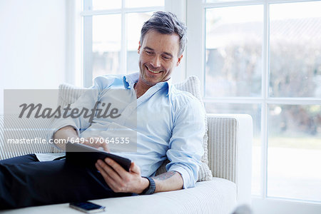 Man relaxing on sofa using digital tablet